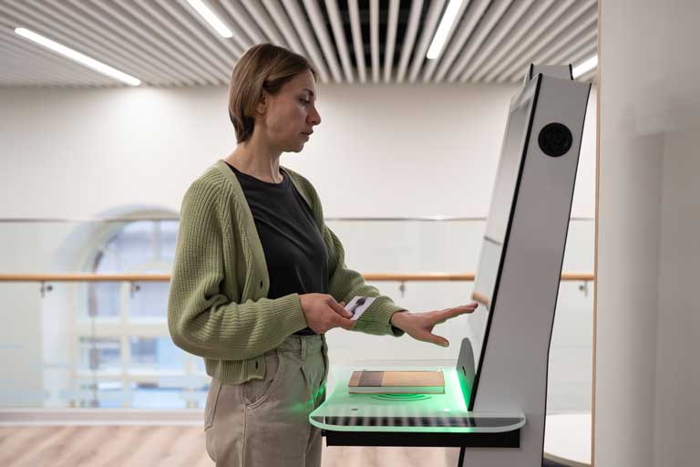 Middle-aged woman registering book in library, using self-service terminal