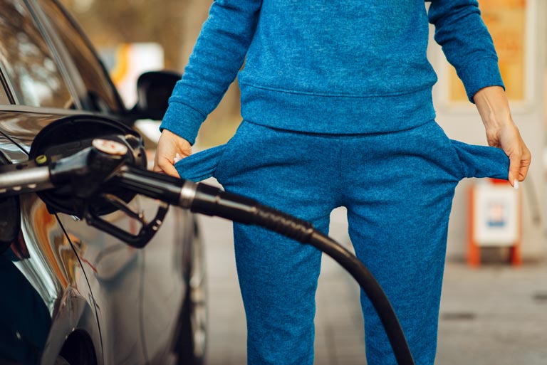 Woman holding empty pockets in front of a gas station while pumping gas