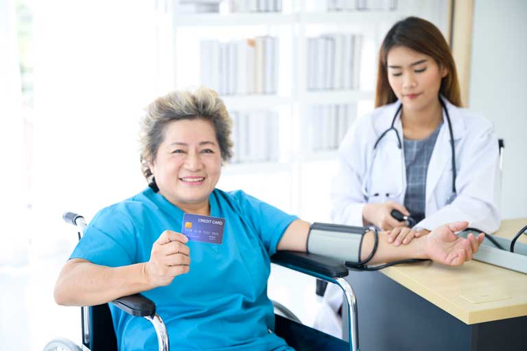 Lady showing a credit card while getting her blood pressure checked by a nurse